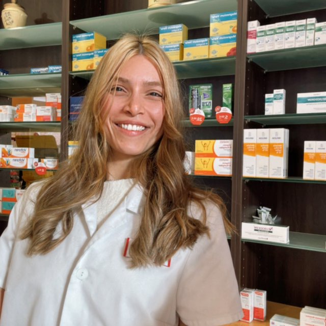 Dr. Leyli Ekhlasmand Kermani in a white pharmacist coat in front of pharmacy shelves